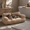 Chat reposant sur un canapé pour chat en tissu bouclette beige, couchage moelleux et élégant dans une salle de bain cosy.