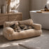 Chat reposant sur un canapé pour chat en tissu bouclette beige, couchage moelleux et élégant dans une salle de bain cosy.