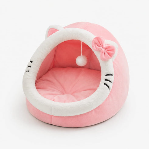 Cocon pour chat rose et blanc en peluche avec coussin moelleux, oreilles décoratives, nœud et pompon suspendu sur fond neutre.