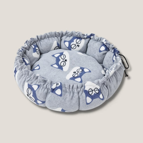 Couffin pour chat en polaire grise, vide, avec motifs de têtes de chat bleues et bord froncé à cordon, présenté en vue de dessus sur fond neutre.