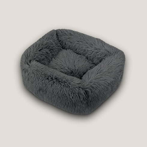 Coussin apaisant pour chat en fourrure anthracite, présenté vide en vue avant sur fond neutre, avec bords moelleux et forme carrée enveloppante.