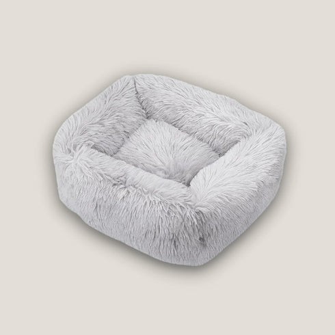 Coussin apaisant pour chat en fourrure gris clair, présenté vide sur fond neutre avec forme carrée moelleuse et bords épais enveloppants.