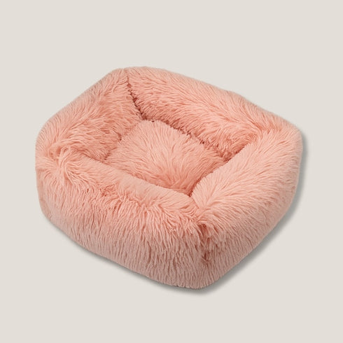 Coussin apaisant pour chat en fourrure rose pastel, forme carrée moelleuse avec bords épais et centre douillet, présenté sur fond neutre.