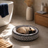 Chat crème endormi dans un coussin pour chaton gris à motifs géométriques avec rebords confortables, installé dans une salle de bain moderne et chaleureuse.