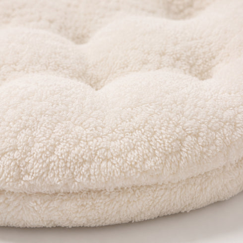 Gros plan sur la texture ultra douce en tissu bouclette d’un coussin pour panier pour chat beige avec rembourrage moelleux et finitions confortables.