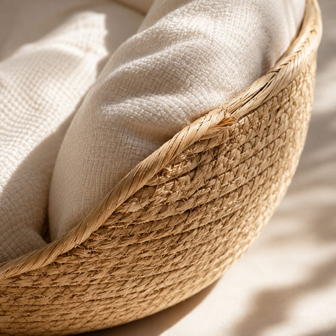 Gros plan sur la texture tressée d’une niche en osier pour chat en imitation osier avec coussin blanc moelleux et finition naturelle dans une lumière douce.
