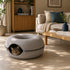 Chat tigré installé dans un couchage donut gris avec ouverture zippée, placé dans un salon chaleureux et lumineux au style naturel.