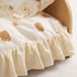 Gros plan sur un lit en bois pour chat avec tissu crème à motifs ours et finitions à volants dans un style doux et cocooning