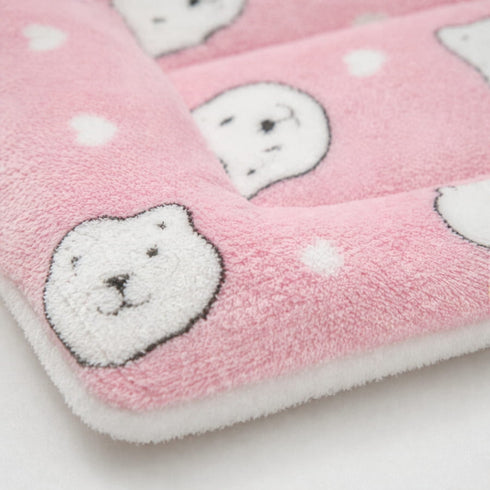 Gros plan sur un petit tapis pour chat rose en peluche douce avec motifs têtes de chat et finition moelleuse sur fond clair