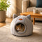 Chat installé dans une grotte pour chat grise en peluche dans un salon, profitant d'un cocon douillet et rassurant pour se reposer en toute tranquillité.