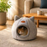 Chat installé dans une grotte pour chat grise en peluche dans un salon, profitant d'un cocon douillet et rassurant pour se reposer en toute tranquillité.
