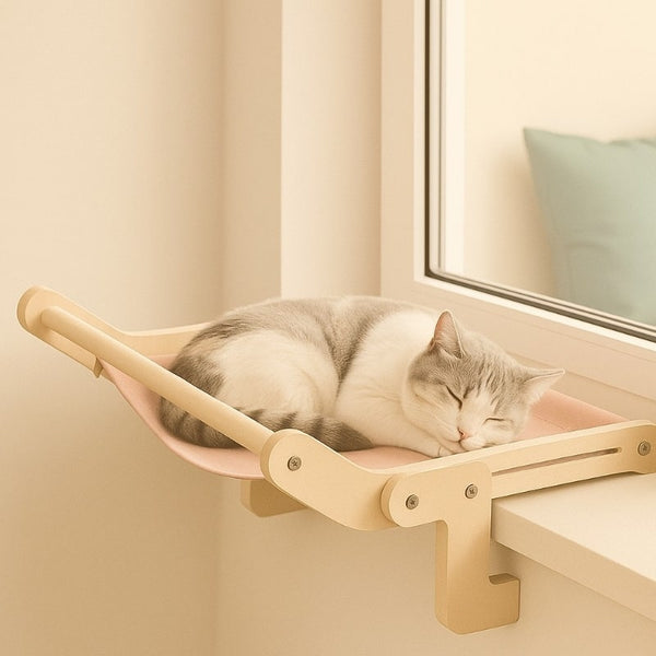 Hamac chat fenêtre sans ventouse en bois clair et tissu rose, fixé sur rebord de fenêtre, avec un chat endormi confortablement installé.