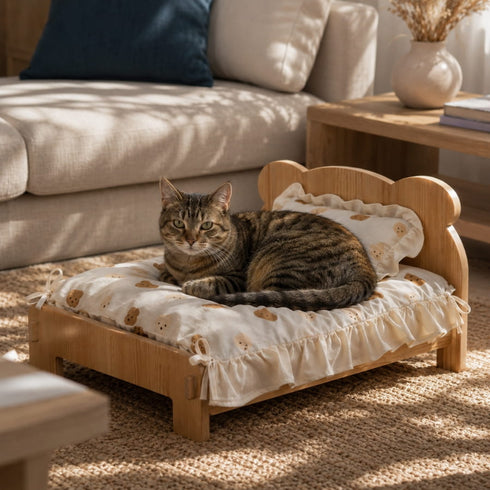 Lit en bois pour chat avec coussin à volants et motifs ours, installé dans un salon lumineux avec un chat tigré au repos