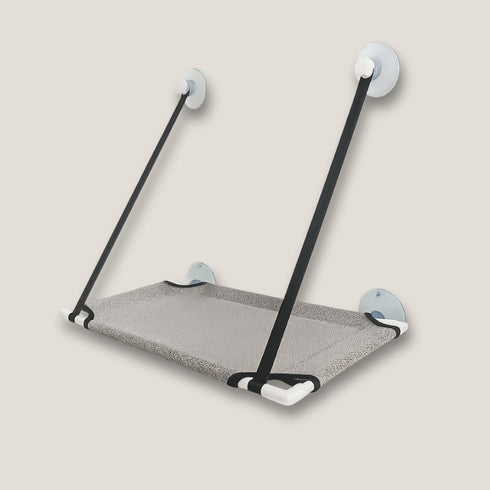 Lit en hauteur pour chat en tissu gris, fixé par ventouses, présenté seul en studio pour montrer la plateforme suspendue et les sangles de maintien.