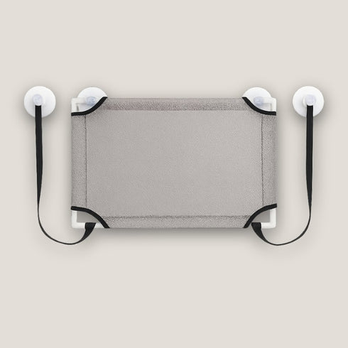 Vue de dessus d’un lit en hauteur pour chat en tissu gris, équipé de ventouses et de sangles, présenté à plat pour montrer la surface de couchage et les fixations.