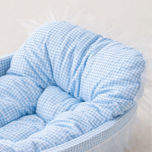 Gros plan sur le rembourrage moelleux et le tissu à carreaux bleus du lit pour chaton avec finition délicate à volants.