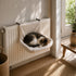 Chat endormi dans un lit radiateur pour chat en peluche beige, suspendu au chauffage pour offrir un couchage chaud et douillet.
