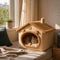 Chat roux endormi dans une maison pour chat beige avec toit moelleux et détails ourson, près d’une fenêtre lumineuse et chaleureuse.