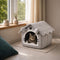 Chat tigré installé dans une maison pour chat grise avec toit en tissu doux, placée près d’une fenêtre lumineuse et apaisante.