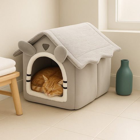Maison à chat grise en tissu près d’une fenêtre, avec un chat roux endormi à l’intérieur.