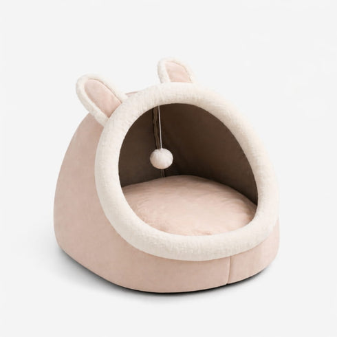 Maison douillette rose pour chat avec oreilles de lapin, coussin moelleux et pompon suspendu, présentée sur fond clair en photo produit