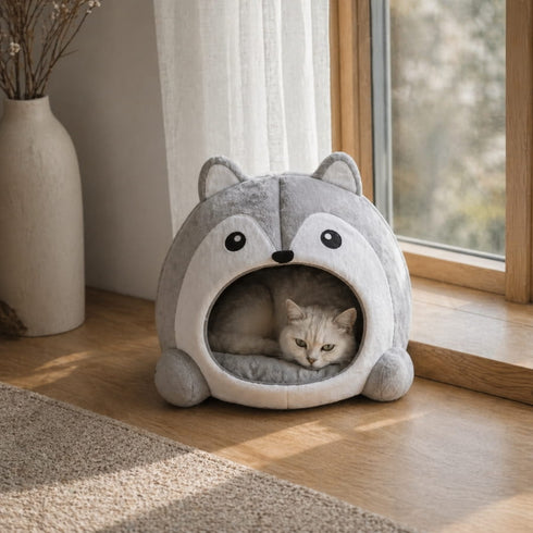 Chat blanc allongé dans une niche pour chat grise en forme de husky, placée près d’une fenêtre lumineuse dans un intérieur cosy.