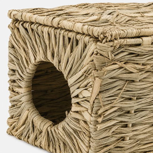 Gros plan sur une petite niche pour chat en osier beige montrant la texture tressée naturelle et l’ouverture ronde du couchage