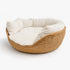 Niche en osier pour chat en imitation osier avec coussin blanc épais et rebords moelleux, présentée sur fond neutre gris clair.