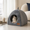 Niche intérieure pour chat grise en tissu doux avec ouverture arrondie, installée dans un salon cosy avec un chat blanc à l’intérieur