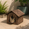Niche isolée pour chat marron avec motifs feuillage et toit rembourré, installée en extérieur avec un chat tigré à l’intérieur