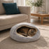 Chat tigré allongé dans un nid pour chat gris ultra doux, installé sur un tapis dans un salon lumineux et chaleureux.