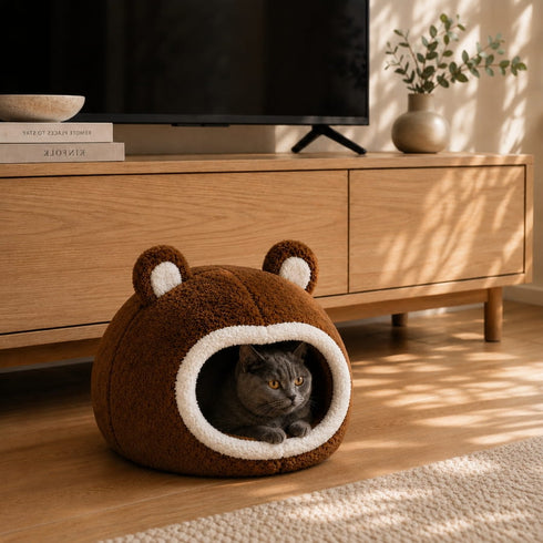 Chat installé dans un panier boule marron ultra doux avec ouverture arrondie et oreilles décoratives, posé dans un salon chaleureux et moderne