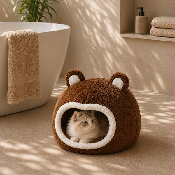 Panier boule marron pour chat avec intérieur moelleux et oreilles décoratives, installé dans une salle de bain lumineuse avec un chat allongé à l’intérieur