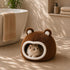 Panier boule marron pour chat avec intérieur moelleux et oreilles décoratives, installé dans une salle de bain lumineuse avec un chat allongé à l’intérieur