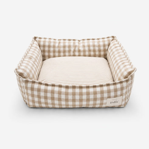 Panier pour chat à carreaux beige avec coussin rayé moelleux et rebords rembourrés sur fond neutre.