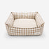 Panier pour chat à carreaux beige avec coussin rayé moelleux et rebords rembourrés sur fond neutre.