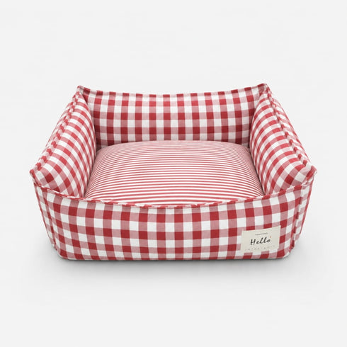 Panier pour chat à carreaux rouge avec coussin rayé moelleux et rebords rembourrés sur fond neutre.