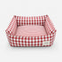 Panier pour chat à carreaux rouge avec coussin rayé moelleux et rebords rembourrés sur fond neutre.
