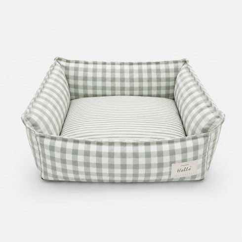 Panier pour chat à carreaux vert avec coussin rayé moelleux et rebords rembourrés sur fond neutre.