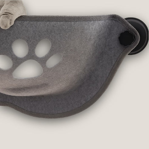 Gros plan du panier pour chat en hauteur en feutre gris fixé à la fenêtre, montrant la ventouse, la couture du bord et le motif patte ajouré.