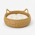 Panier à chat imitation osier beige avec coussin crème moelleux et poignées intégrées pour un couchage confortable et élégant.