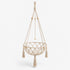 Panier pour chat suspendu en macramé beige avec pompons et perles en bois, idéal pour créer un espace repos bohème et élégant.