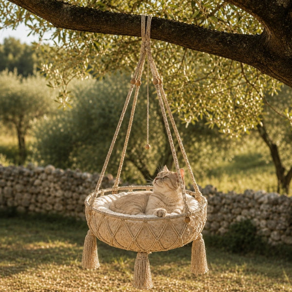 Panier pour chat suspendu en macramé beige avec coussin moelleux, accroché à un arbre pour offrir un espace repos bohème et confortable.