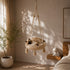 Chat installé dans un panier pour chat suspendu en macramé beige avec pompons décoratifs, parfait pour un coin repos bohème et apaisant.