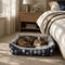 Chat tigré reposant dans un panier chaud pour chat bleu et gris, placé au pied d’un lit dans une chambre cosy et apaisante.