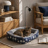 Chat tigré installé dans un panier chaud pour chat bleu à motifs, dans un salon chaleureux avec fauteuil et lumière douce.