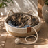 Chat tigré allongé dans un panier en rotin pour chat en imitation rotin avec corde de jeu intégrée et coussin bleu, posé sur une terrasse sur un sol en bois.