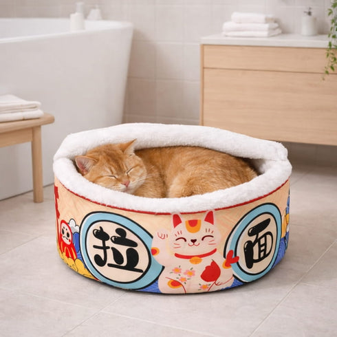 Chat roux endormi dans un panier fermé pour chat rond, doublé de peluche blanche, motif multicolore, en salle de bain.