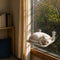 Chat blanc allongé sur un perchoir de fenêtre beige fixé par ventouses, idéal pour observer l’extérieur et se reposer au soleil.