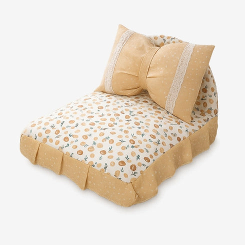 Petit lit pour chat beige avec coussin en forme de nœud, tissu à motifs fruits, présenté en studio sur fond blanc.